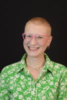 person with short hair and glasses smiling at camera wearing green blouse with white flowers