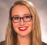 Smiling woman with brown/blonde hair, glasses, and red lipstick.