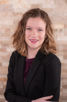 Picture of woman with curly brown hair, smiling at camera. She is wearing a black blazer and burgundy top. 