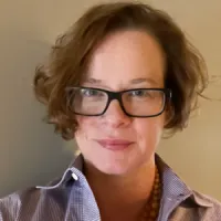 Woman with curly brown hair wearing glasses and collared shirt.