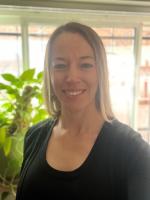 Smiling woman with brown hair and wearing a black shirt in front of a large plant.