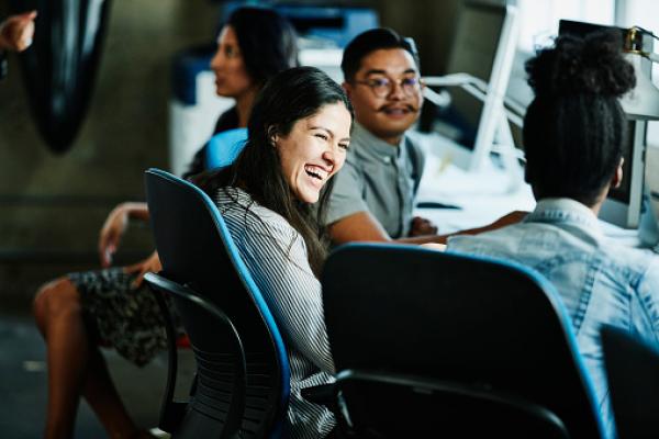 A woman sitting at a conference table, smiling and laughing with other people