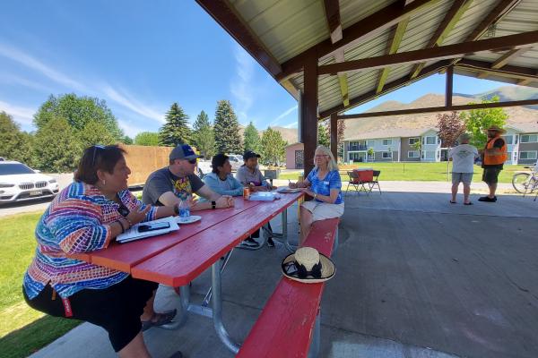 Photograph of five people sitting around an outdoor picnic table talking.