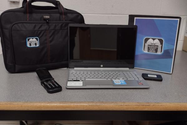 Photograph of the toolkit. Photo shows a black bag, Chrome book, cell phone, flash drive and folder of resources.