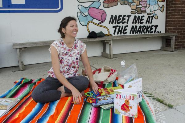 Women sits on blanket with books around her.