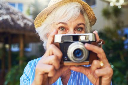 senior lady with straw hat and smiling eyes getting ready to snap a picture with her digital camera