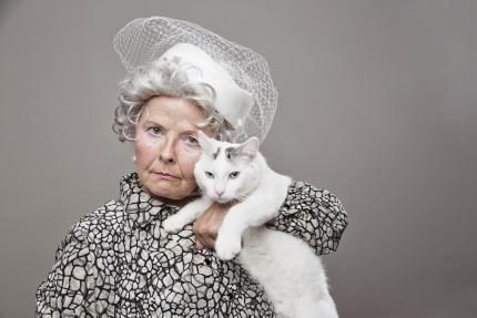 Eccentric senior lady wearing vintage hat poses with her cat