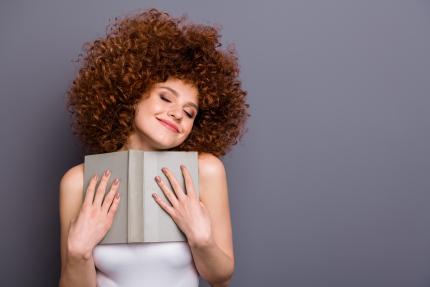 college age girl with wild curly red hair embraces a favorite book with ecstatic facial expression