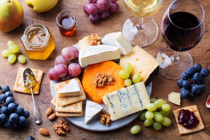 assortment of cheese fruit and wine on a wooden surface