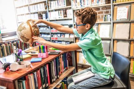 schoolboy studying in the library using a globe