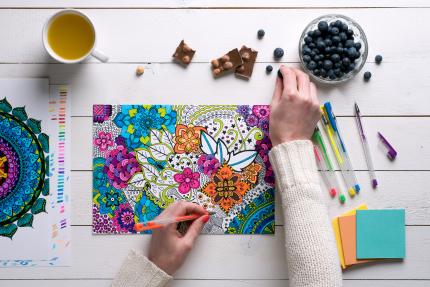 photo of female hands coloring an adult coloring book with an array of supplies and snacks