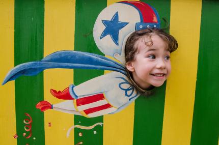 like a cannonball little girl pretending to fly like a cannon ball out of a cannon using a face-cutout at a circus
