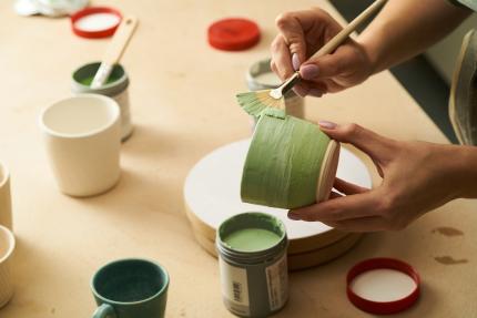 Close-up of painting clay mug with green paint