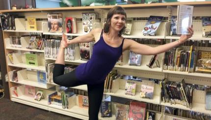 Woman holds a book while balancing in dancer pose at the Fredericton Public Library