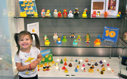 Photograph of a child smiling in front of a case full of different rubber duckies.