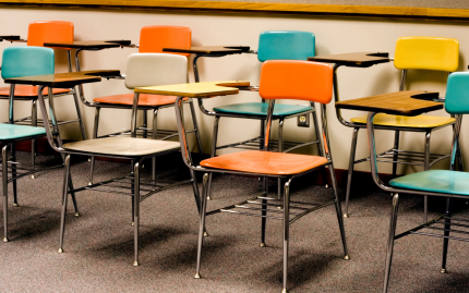 Photograph of two rows of empty desks inside a classroom.