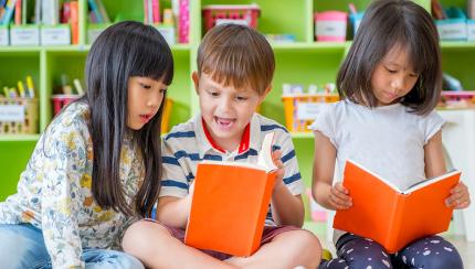 Three children sitting down and looking at books Three children sitting down and looking at books