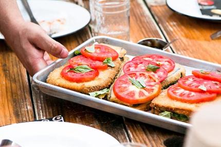 Hand putting pan of a tomato dish on table