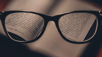 Glasses magnifying the text on the page of a book