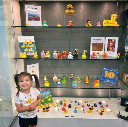 Photograph of a child smiling in front of a display case full of different rubber duckies.