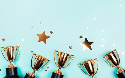 Photograph of gold trophies against a blue background with stars.
