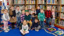 group of children sit in front of bookshelves