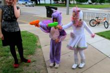 Children dressed as superheroes shoot squirt guns at a target.
