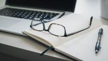 a laptop, eyeglasses, open notebook on a desk