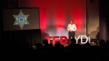 Speaker at TedxYDL next to PowerPoint presentation 