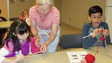 Student getting help from teacher with a another student knitting Student getting help from teacher with a another student knitting