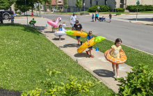 Photograph shows children outside playing a sidewalk chalk game with pool floaties on.