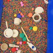 Photograph of a sensory tub filed with colorful beads and other sensory items.