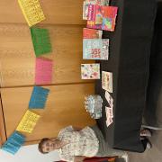 Photograph of presenter and volunteer, Ana H, standing next to a table with craft books and a completed papel picado