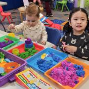 Two toddlers play at a table with kinetic sand