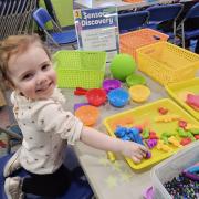 A smiling toddler plays with kinetic sand