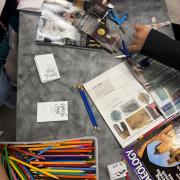 A photo of a table with various craft materials, magazines, and hands cutting out pictures