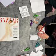 A photo of a table with various craft materials, magazines, and hands writing on paper