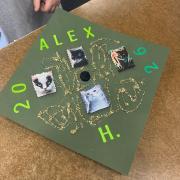 Grad cap decorated with glitter glue and four photos of cats. Text reads Alex H 2026