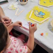 A child glues popsicle sticks onto a honeycomb craft