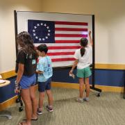Photograph of three people engaging with game puzzle and Betsy Ross American flag