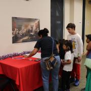 Photograph of a group of patrons engaging in a puzzle game with a painting of the signing of the Declaration of Independence on the wall