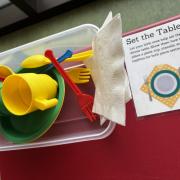 A photograph of the Set the Table station with napkins and plastic dishes.