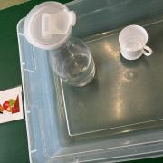A photograph of the water pouring station with a plastic water bottle and cups.