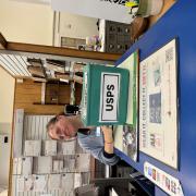A person sitting in a post office with a green box labeled USPS