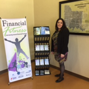 Photograph of library staff posting with Financial Fitness banner and resources bookshelf.