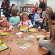 Children sit around a table and create stained glass using CD's.