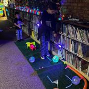Photograph of kids participating in Glow Golf next to a bookshelf
