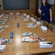 Magazines, boxes and supplies are spread across a long table.
