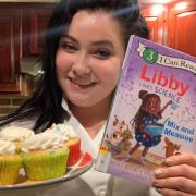 Screenshot from read-aloud video. Libby Ortiz is pictured holding the book "Libby Loves Science: Mix and Measure" by Kimberly Derting and a plate of cupcakes.
