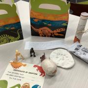 Photograph of Dinovember contents: Dinosaur boxes, clay, egg, three small dinosaur toys and certificate of adoption.